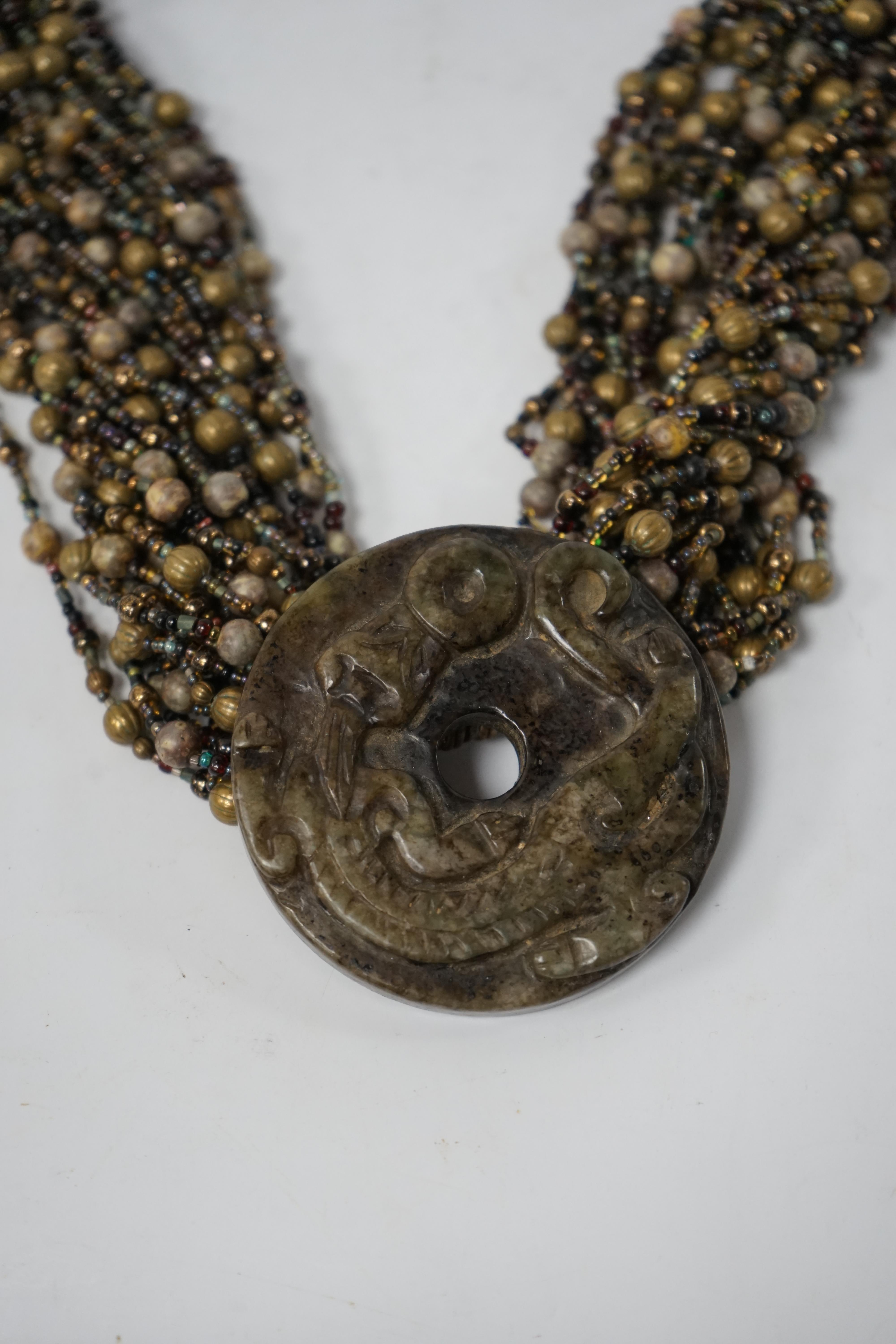 A Chinese multi bead necklace with carved bowenite ‘dragon’ pendant, disc 6cm in diameter. Condition - fair to good